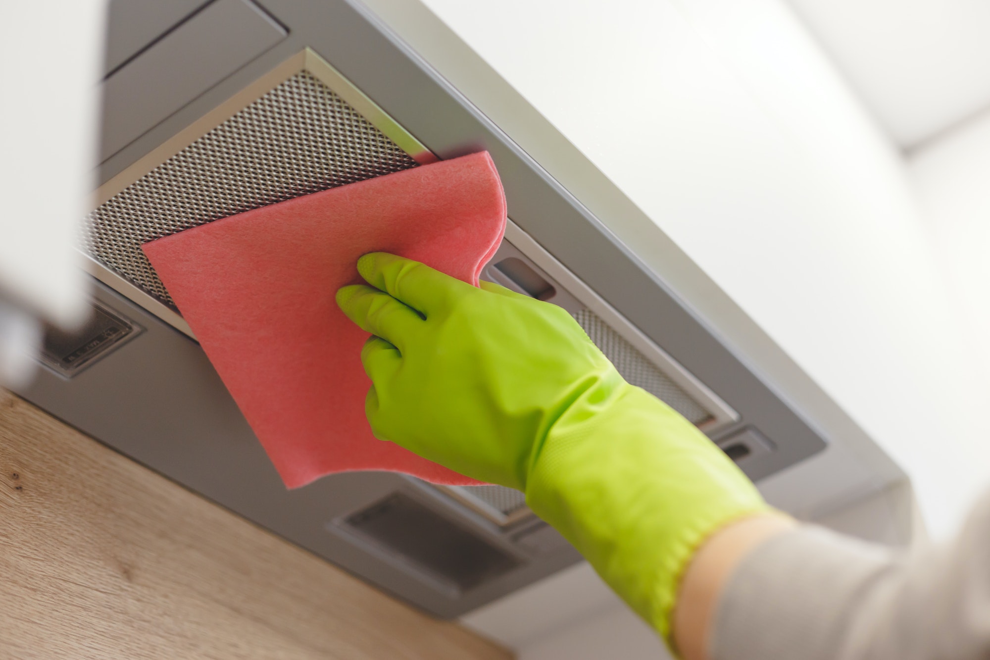 Cleaning domestic cooker hood grid with pink cloth fiber napkin.